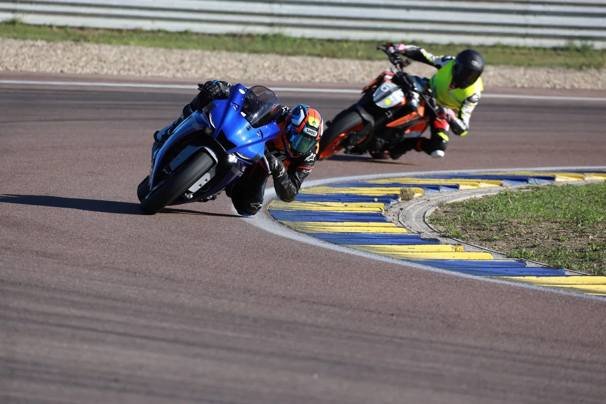 An instructor on a Yamaha R1 leaned over at the kerb, with a participant in a hi-vis vest right behind – in guided race track training the group follows the instructor's line.