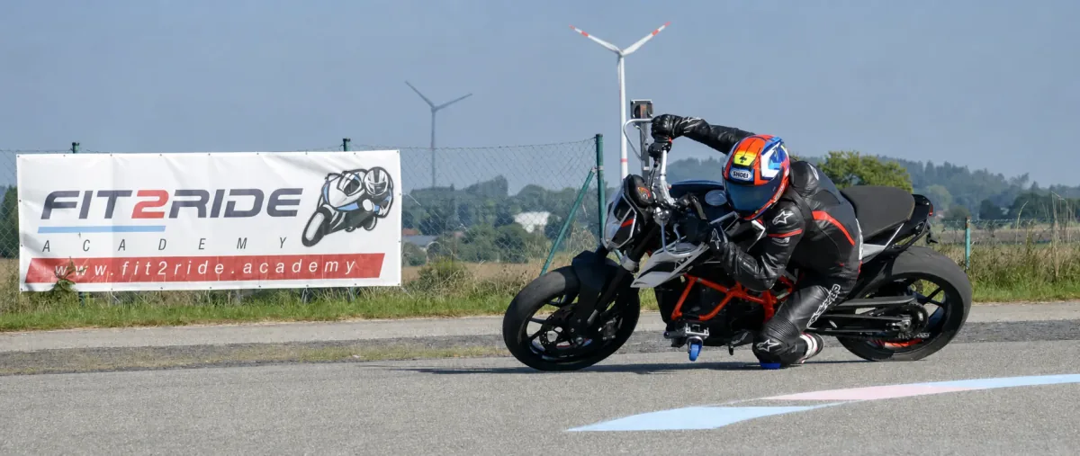 Dynamics without risk: a participant trains hanging off and knee dragging safely on the motorcycle with outriggers.