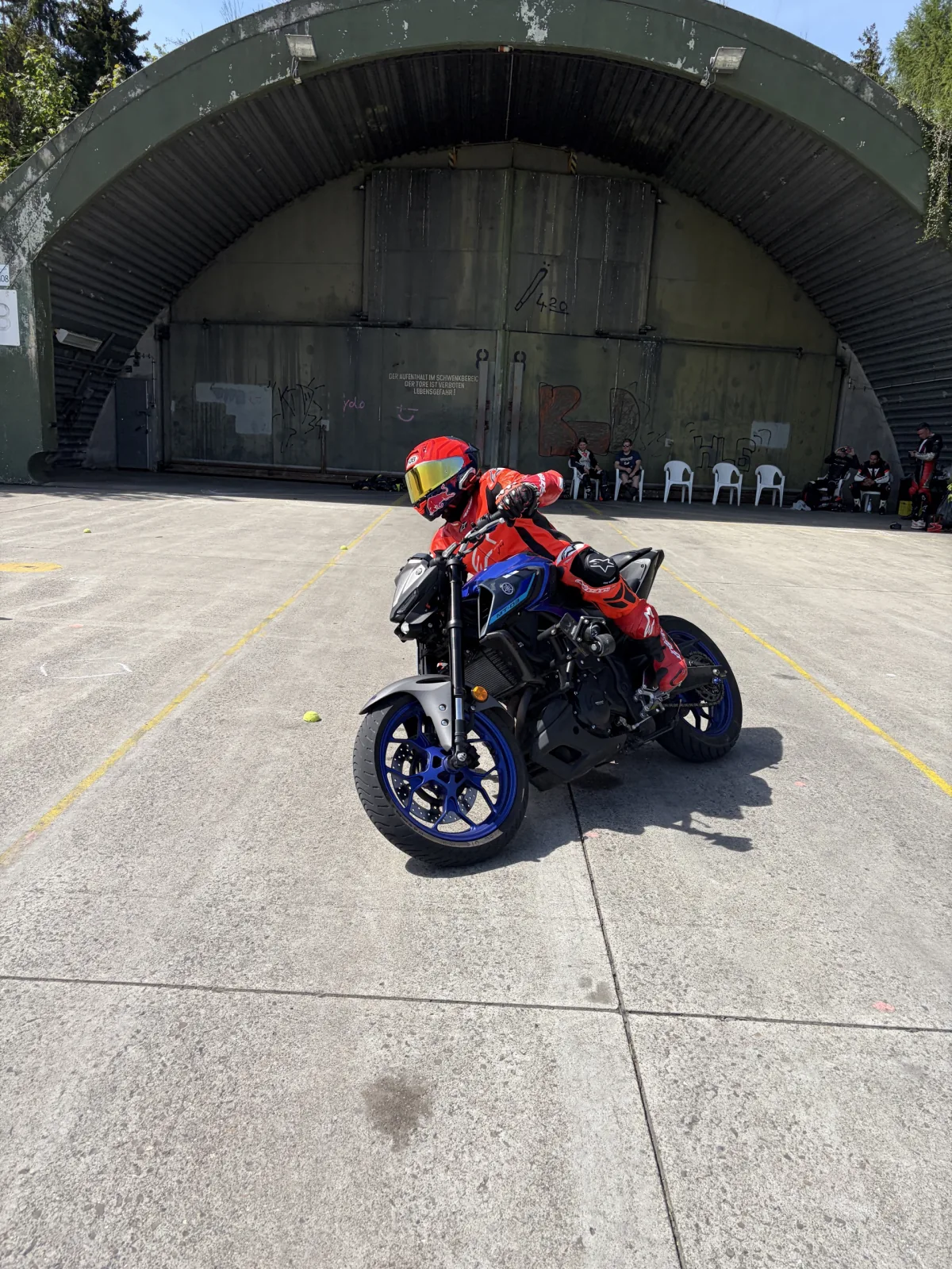 Training day on the practice area: one participant rides an exercise while the others wait in front of the hangar.