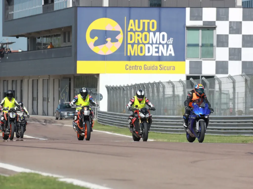 Eine geführte Gruppe von Teilnehmern in Warnwesten folgt dem Instruktor auf der Rennstrecke vor dem Autodromo di Modena.